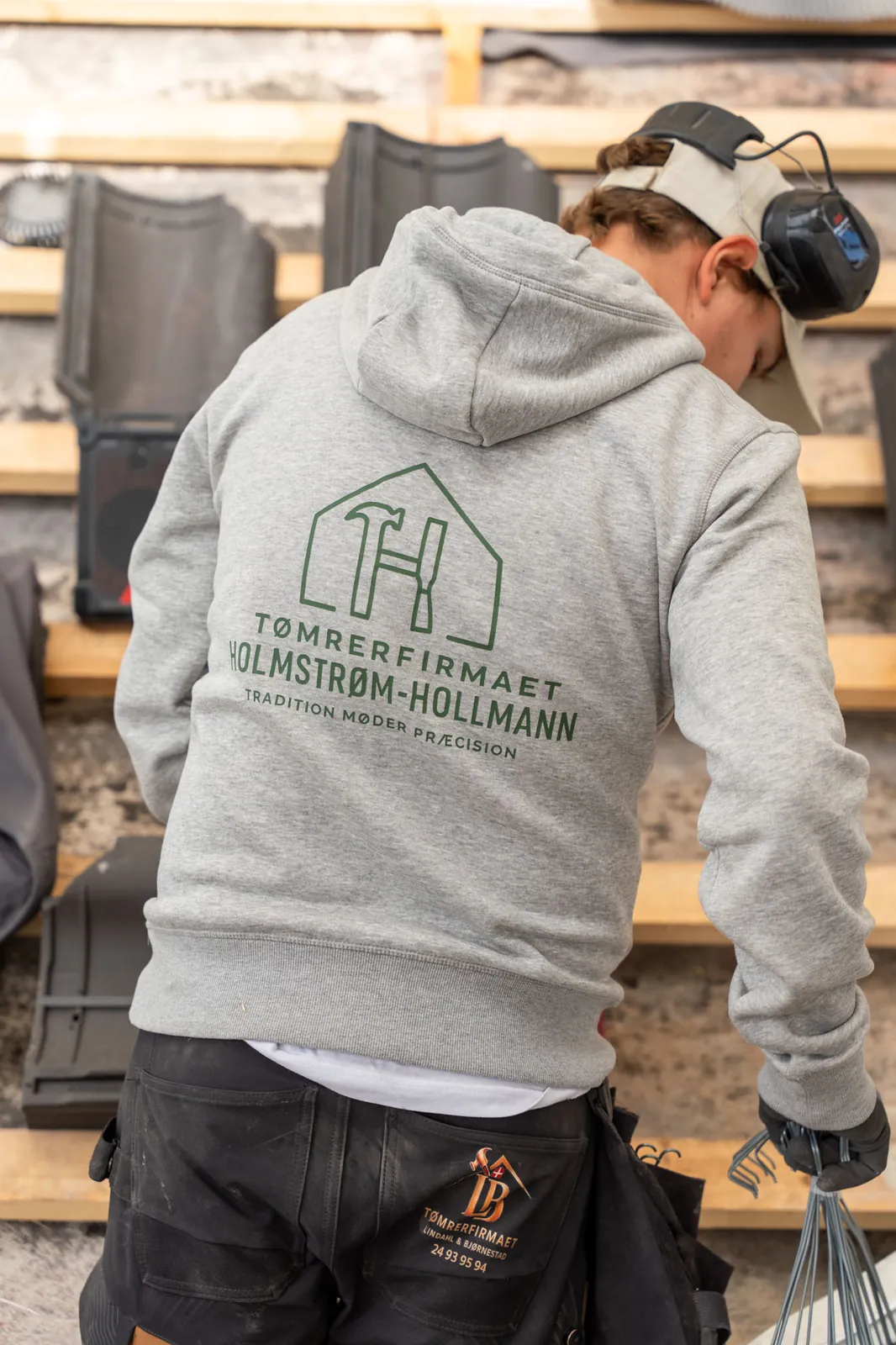 Tømrer i hættetrøje med Tømrerfirmaet Holmstrøm-Hollmanns logo på ryggen